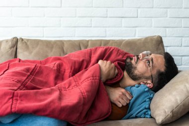 Mutlak yalnızlık. Yalnız, üzgün ve sefil hissederken üzgün üzgün bir adamın kanepeye uzanıp battaniyeye sarılışının yan görüntüsü. Depresyon zihinsel sağlık sosyal sorunu