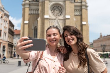 Moda kıyafetleri içinde gülümseyen iki güzel hippi kız. Sokakta poz veren kaygısız seksi kadınlar. Gün batımında akıllı telefondan turist olarak kendi fotoğraflarımı çekiyorlar..