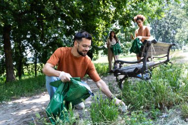 Birlikte parkı temizleyen, çöp toplayan ve çöp torbası tutan genç gönüllüler. Sorumlu ebeveynler ve arkadaşlar çocuklar doğada oynamaya gelmeden önce parkı çöpten temizliyorlar..