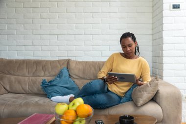 Genç Afrikalı Amerikalı kadın, oturma odasında kanepede rahatça oturup internet alışverişi yapıyor tablet üzerinde, mutlu çift ırklı kadınlar kanepede dinleniyor ve modern ped cihazına mesaj atıyor.