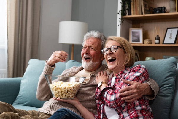 Old retired age couple watching TV at home, old mature couple cheering sport games competition together with laugh smile victory on sofa couch at living room home. Senior man and woman movie night.