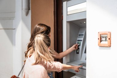 İki güzel turist kadın, şehir merkezindeki ATM makinesiyle banka kartından para çekiyor. İki gezgin arkadaş öğle yemeği ve kahve için para çekiyor.