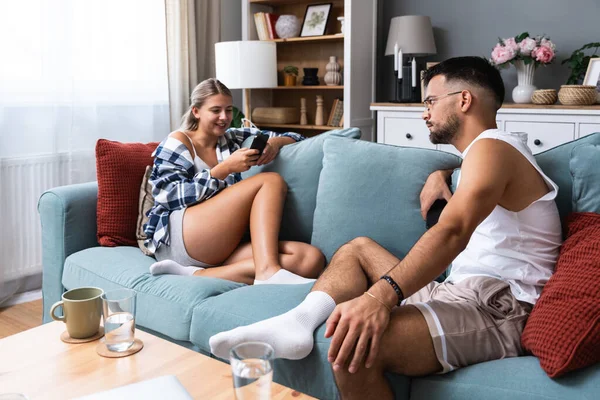Man and woman online messaging social media and network addiction, flirting and jealousy, ignoring each other at home while sitting on sofa. Young couple ignorance and relationship difficulties.