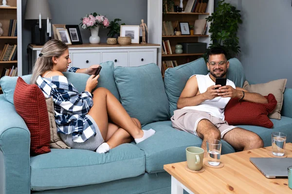 Man and woman online messaging social media and network addiction, flirting and jealousy, ignoring each other at home while sitting on sofa. Young couple ignorance and relationship difficulties.