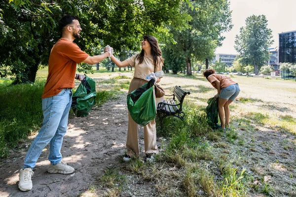 Group of young conscious activists collect and clean up trash from the park to keep the environment clean. Friends reduce pollution of green areas in the city after irresponsible and arrogant citizens