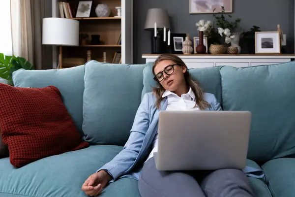 Young business woman fell asleep on sofa while working on laptop. Overworked tired woman tired of working on computer from home office sleeping with laptop on lap.