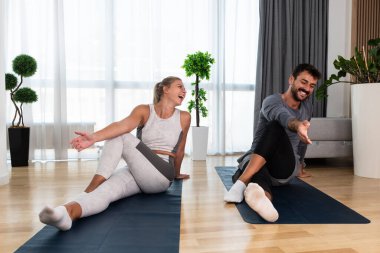 Çift birlikte egzersiz yapıyor. Spor giyimli kadın ve erkek evde spor yapıyor. Yoga dersleri alan partnerler yoga minderleri üzerinde kaslarını esneten iş stresinden sonra nefes alma egzersizleri yapan partnerler.
