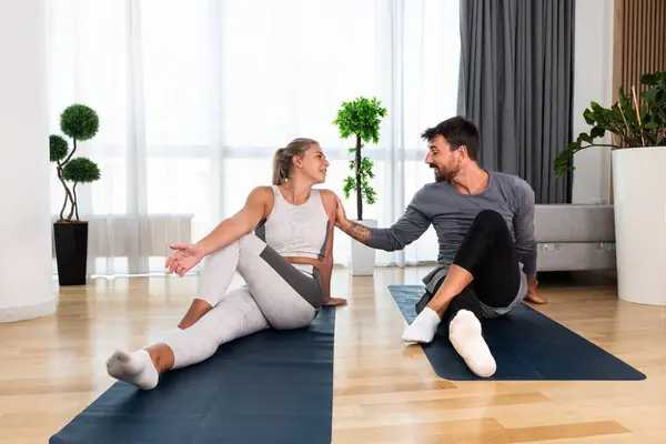 Couple exercising together. Man and woman in sportswear doing workout at home. Partners doing yoga class in the apartment on yoga mats stretching muscles breathing exercises after stress at work