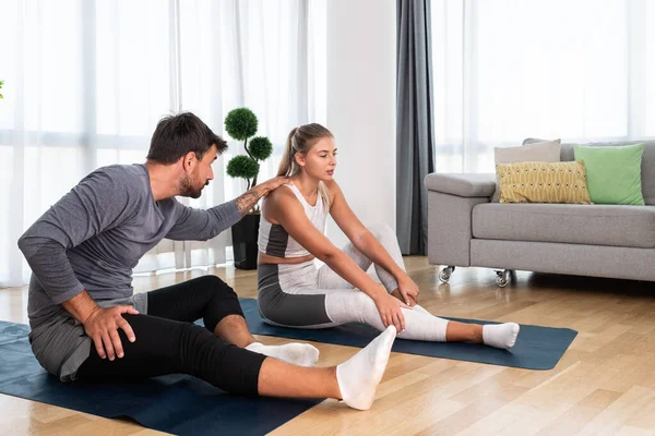 Couple exercising together. Man and woman in sportswear doing workout at home. Partners doing yoga class in the apartment on yoga mats stretching muscles breathing exercises after stress at work