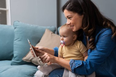 Mother, baby and tablet on sofa watching educational video online on streaming service in home. Love, family time and woman with girl child smile on couch to watch kids movie or cartoon on website.