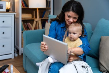 Mother, baby and tablet on sofa watching educational video online on streaming service in home. Love, family time and woman with girl child smile on couch to watch kids movie or cartoon on website.