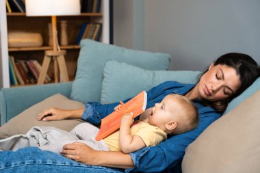 Genç anne bebeğine masal kitabı okuduktan sonra uyuyakaldı. Kucağında çocuğuyla uyuyan yorgun anne akşam vakti çocuğuna kitap okumaya çalıştı. Bekar anne kavramı.