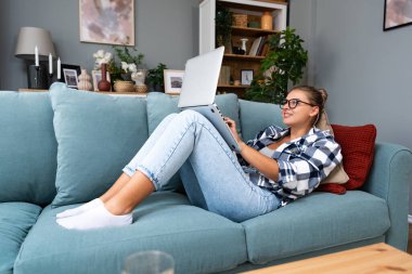 Genç başarılı serbest çalışan iş kadını. Kanepede yatıp dizüstü bilgisayarla çalışıyor. Milenyum yeniyetme kadın internette geziniyor, uzaktan kumandalı iş, küçük bir şirket sahibi..