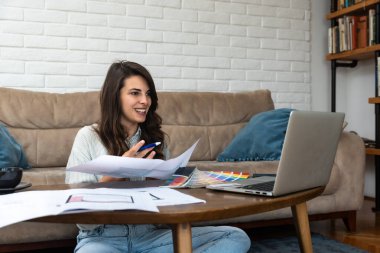 Yeni bir proje üzerinde çalışan serbest çalışan genç bir iç mimar kadın. İşletme sahibi kadın mimar kağıt planları ve dizüstü bilgisayar çözümlerini kontrol ediyor.