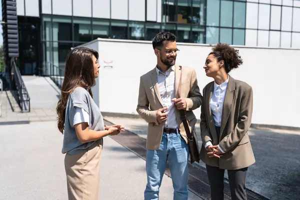 Group of successful young business people, leaders in marketing and motivation, stand in front of office building and consult before a meeting with employees. HR communication in companies concept