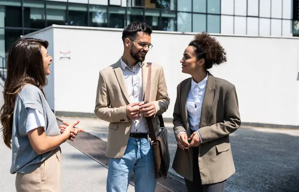 Group of successful young business people, leaders in marketing and motivation, stand in front of office building and consult before a meeting with employees. HR communication in companies concept