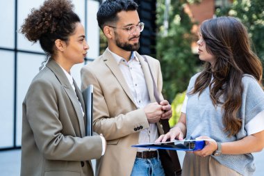 Ofis binasının dışında çeşitli genç iş adamları yeni inşaat planını çözen erkek ve kadını tartışıyor ve konuşuyorlar.