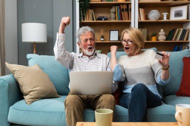 Mutlu, yaşlı, emekli çift online alışveriş için kredi kartı ve dizüstü bilgisayar kullanıyor, internetten alışveriş yapıyor, tatil için turu seçiyor, banka başvurusuyla ödeme yapıyor, finansal hizmet yapıyor.