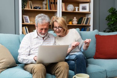 Mutlu, yaşlı, emekli çift online alışveriş için kredi kartı ve dizüstü bilgisayar kullanıyor, internetten alışveriş yapıyor, tatil için turu seçiyor, banka başvurusuyla ödeme yapıyor, finansal hizmet yapıyor.