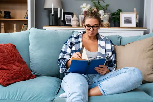 stock image Young happy self loved independent woman lady reading a book at home, sitting on sofa, enjoying free time. Strong satisfied female reader read a story, spending quality time on her day off from work.