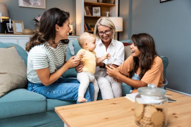 Mutlu bir aile. Büyükanne, anne, teyze ve küçük bebek evde eğleniyor. Yeni doğan çocuğu ziyaret eden akrabalar.