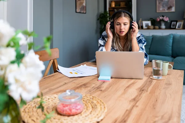 Happy woman wearing wireless headphones working on laptop at home office. Business female startup small company owner work on internet on computer.