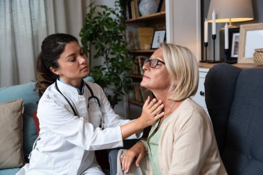 During a home visit to an elderly patient, a young endocrinologist doctor checks her thyroid gland by feeling her neck with her hands. Senior women endocrinology health care clipart