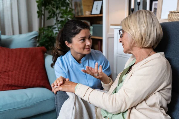 Caring young woman nurse help old granny during homecare medical visit, female caretaker doctor talk with elder lady give empathy support encourage patient sit on sofa older people healthcare concept