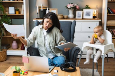 Anne bilgisayarda çalışıyor ve bilgisayar kamerasıyla konuşuyor. Bebek oynarken iş ortaklarıyla görüntülü konuşma yapıyor. Kadın evden çalışıyor ve çocuklara bakıyor..