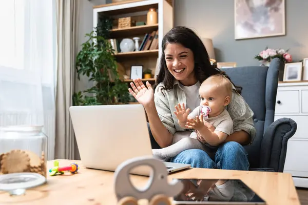 Stay at home mom working remotely on laptop while taking care of her baby. Young business mother on maternity leave trying to freelance by the desk with toddler child. Global work on computer