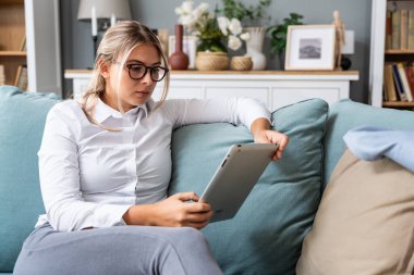 Genç iş kadını kripto döviz tüccarı ana ofiste oturuyor ve kanepede otururken tablet üzerinde çalışıyor. Serbest çalışan kadın küresel iş adamı küçük şirket sahibi evden internet üzerinde çalışıyor.