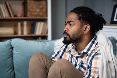 Young depressed African American man sitting on sofa with crossed arms. Racism victim for skin color black male suffering from depression after being fired from work Job lost and mental health concept