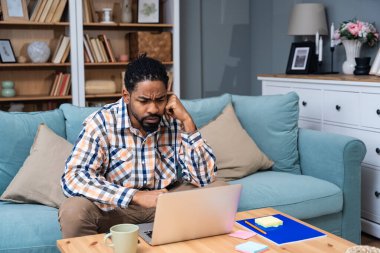 Young freelance business man or exchange student working remotely from his home office on laptop computer. African American work on new web project using internet for online job to increase earnings