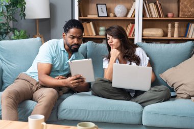 Genç çift iş ortakları evdeki ofiste birlikte çalışıyorlar, kanepede dizüstü bilgisayar ve tablet kullanıyorlar. Küçük şirket sahipleri çalışıyor, internet girişimcileri birbirlerine fikirlerini gösteriyorlar.