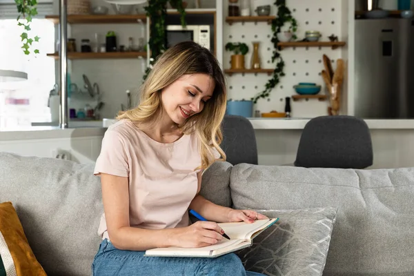Young woman sitting on the sofa writing down the guest list of her friends whom she will invite to her bachelorette party for her wedding. Creative girl writes down ideas make a list of things to do
