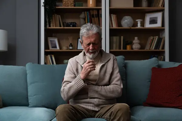 Elderly aged senior man sitting alone in the dark of his apartment depressed and sad after the loss of his wife who passed away. Poor mental health after the death of a loved one, negative emotions.
