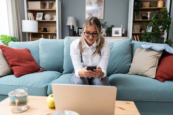 Genç kadın doktor, akıllı telefondaki mesajlarını kontrol eden kadın doktor bilgisayarındaki video görüşmesine web kamerası ve hastasıyla başlamadan önce. Teletıp kavramı