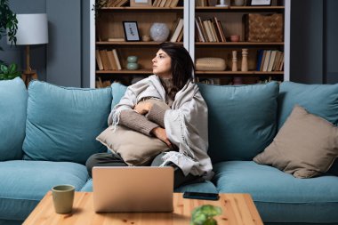 Kafkasyalı üzgün kadın depresyonda kanepede oturuyor. Zihinsel çöküntüden muzdarip genç bir bayan, depresyona girmiş, battaniyeye sarılmış, evinde sessizce oturuyor..