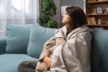 Kafkasyalı üzgün kadın depresyonda kanepede oturuyor. Zihinsel çöküntüden muzdarip genç bir bayan, depresyona girmiş, battaniyeye sarılmış, evinde sessizce oturuyor..