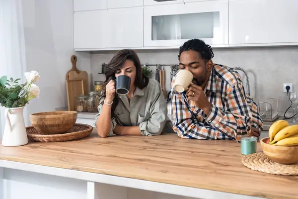 Stock image Young couple drinking coffee together in the kitchen on early morning before they go to the work. Emotional people spending free time with tea and conversation.