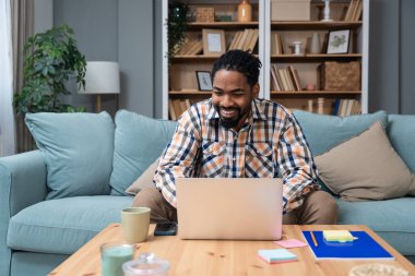 Odaklanmış genç Afrikalı Amerikalı serbest iş adamı çalışması internetten bilgisayardan webinar podcast izliyor eğitim kursu konferansını dinliyor notlar alıyor çalışma masasında e-öğrenim konseptine oturuyor.