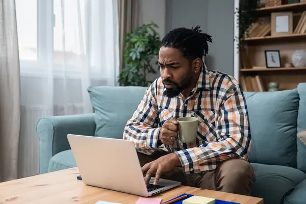 Focused young African American freelance businessman study online watching webinar podcast on laptop listening learning education course conference call make notes sit at work desk e-learning concept