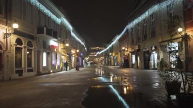 Sırbistan 'ın Novi Sad kentinde binalar ve insanların kar altında yürüdüğü soğuk kış gününde kent hayatının gece görüntüsü. 