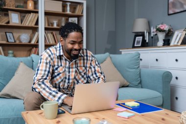 Kulaklıklı genç Afro-Amerikalı bir adam dizüstü bilgisayar ve akıllı telefon kullanarak internet üzerinden arıyor. Kanepenin üzerinde oturmuş, web kamerasındaki ana konuşuyor. İnternetteki iş ürünleri stratejisi toplantısı.