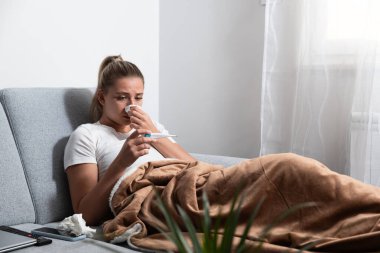 Battaniyeye sarılı genç hasta bir kadın burnunu kağıt mendille siler, hastalanır çünkü evinde ısıtma ve şehrin ısıtma sisteminde bozulma için parası yoktur..