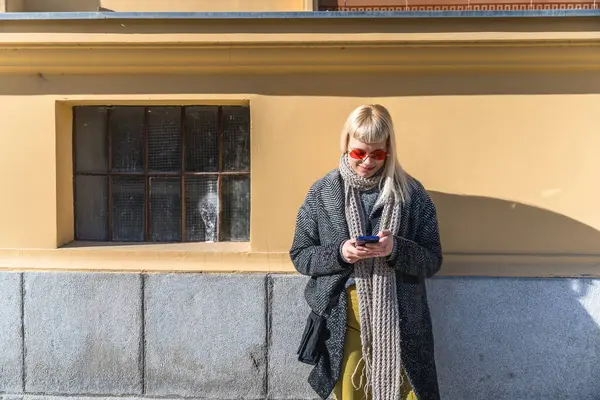 Havalı gözlüklü hippi bir kadın şehir sokaklarının duvarına yaslanmış cep telefonu sohbetini sosyal ağda yapıyor. Kentsel yaşam tarzı kavramı.