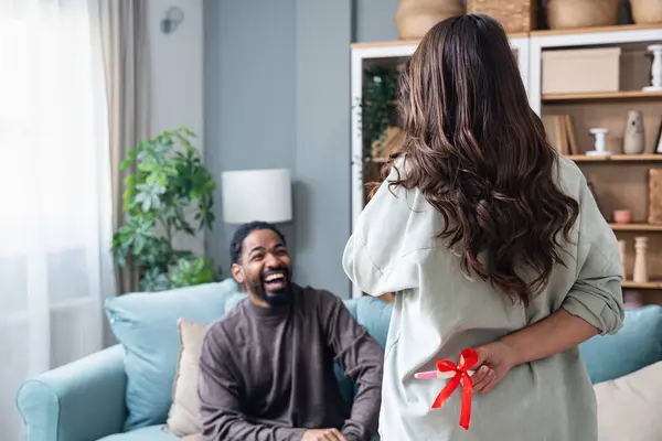 Woman hiding positive pregnancy test from her spouse for a surprise. Young couple man and pregnant woman at home wish come through to become a parents. Surprising effect concept