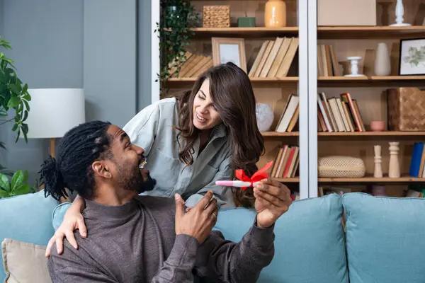 Woman hiding positive pregnancy test from her spouse for a surprise. Young couple man and pregnant woman at home wish come through to become a parents. Surprising effect concept