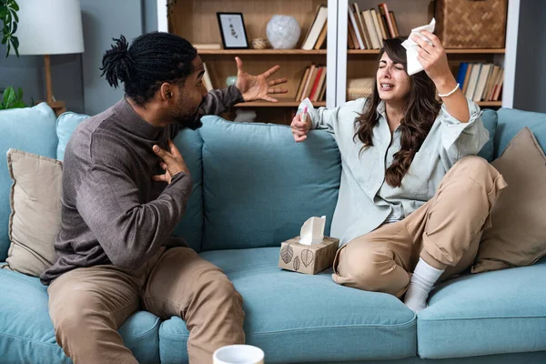 Unhappy young woman sitting on sofa with pregnancy test, African American husband screaming at her, indoors. Millennial family having conflict over unexpected childbearing, argue over results