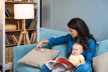 Genç anne, evdeki kanepede otururken bir masal kitabı okuyarak yeni doğmuş bebeğini eğlendirmeye çalışıyor. Bir kadın, küçük çocuğuyla eğlenmek için kitap okurdu..